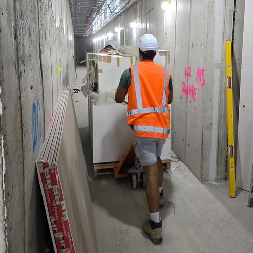 Two builders pushing a Superior Kitchen kitchen on a trolley along a passage way in an under construction apartment building for installation.