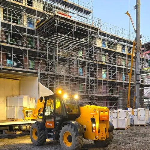 A yellow telehandler is lifting Superior Kitchen kitchens on pallets in front of an under construction apartment building.